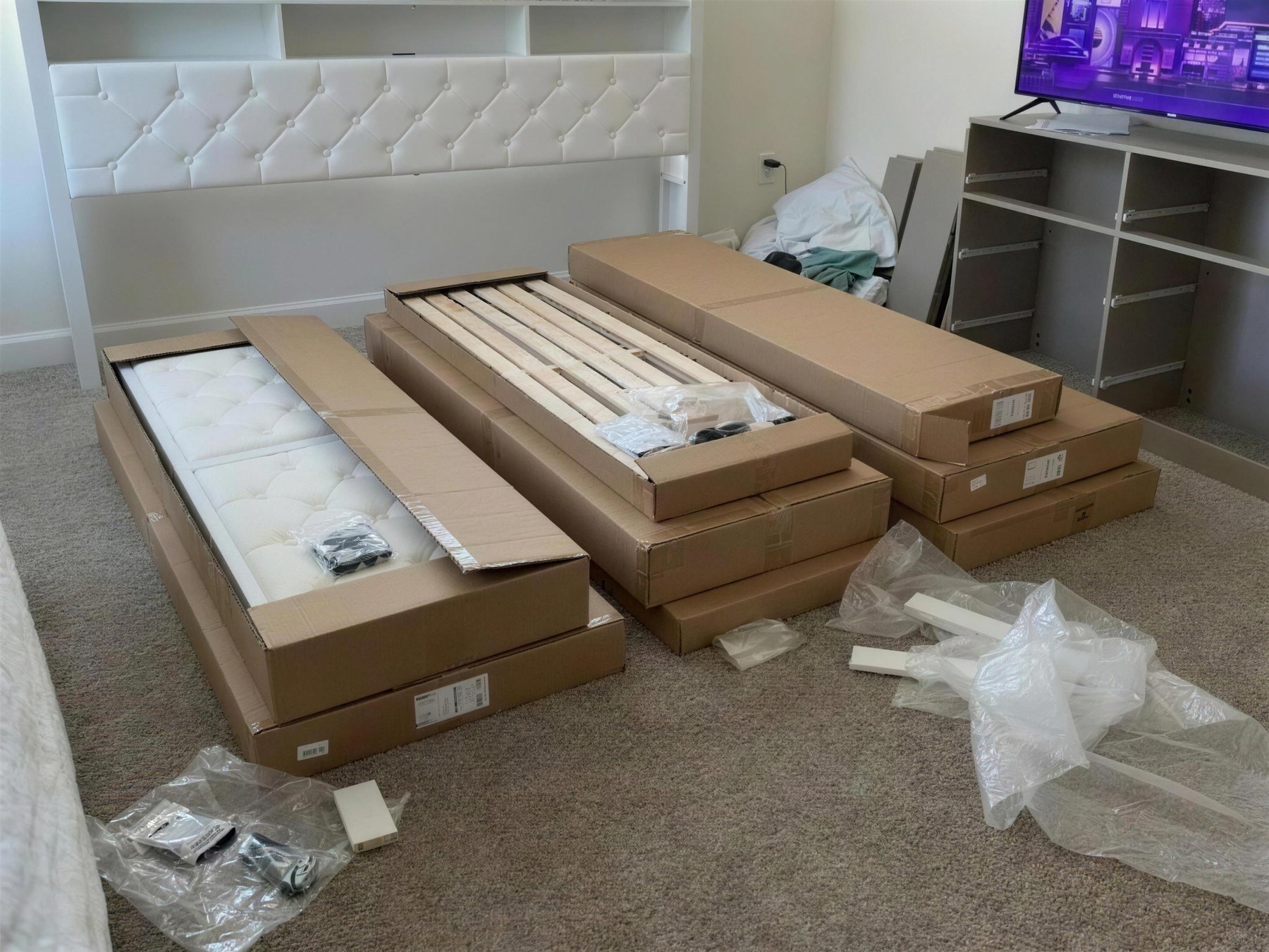 A rental bedroom with flat cartons and a part-built bed frame on the floor.