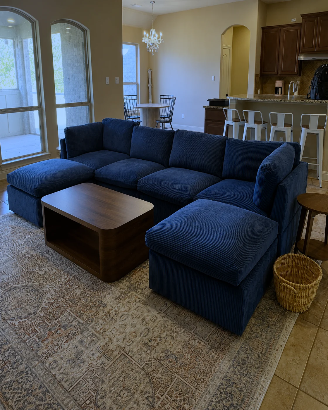 A navy modular sectional and its ottoman, assembled on a rug in an open-plan living room.
