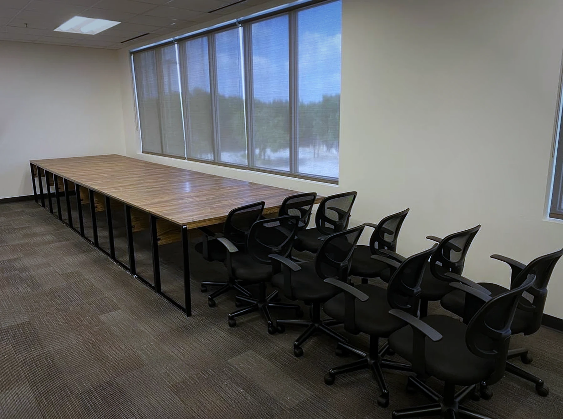 A long run of office desks with black mesh chairs, installed beside a window wall.