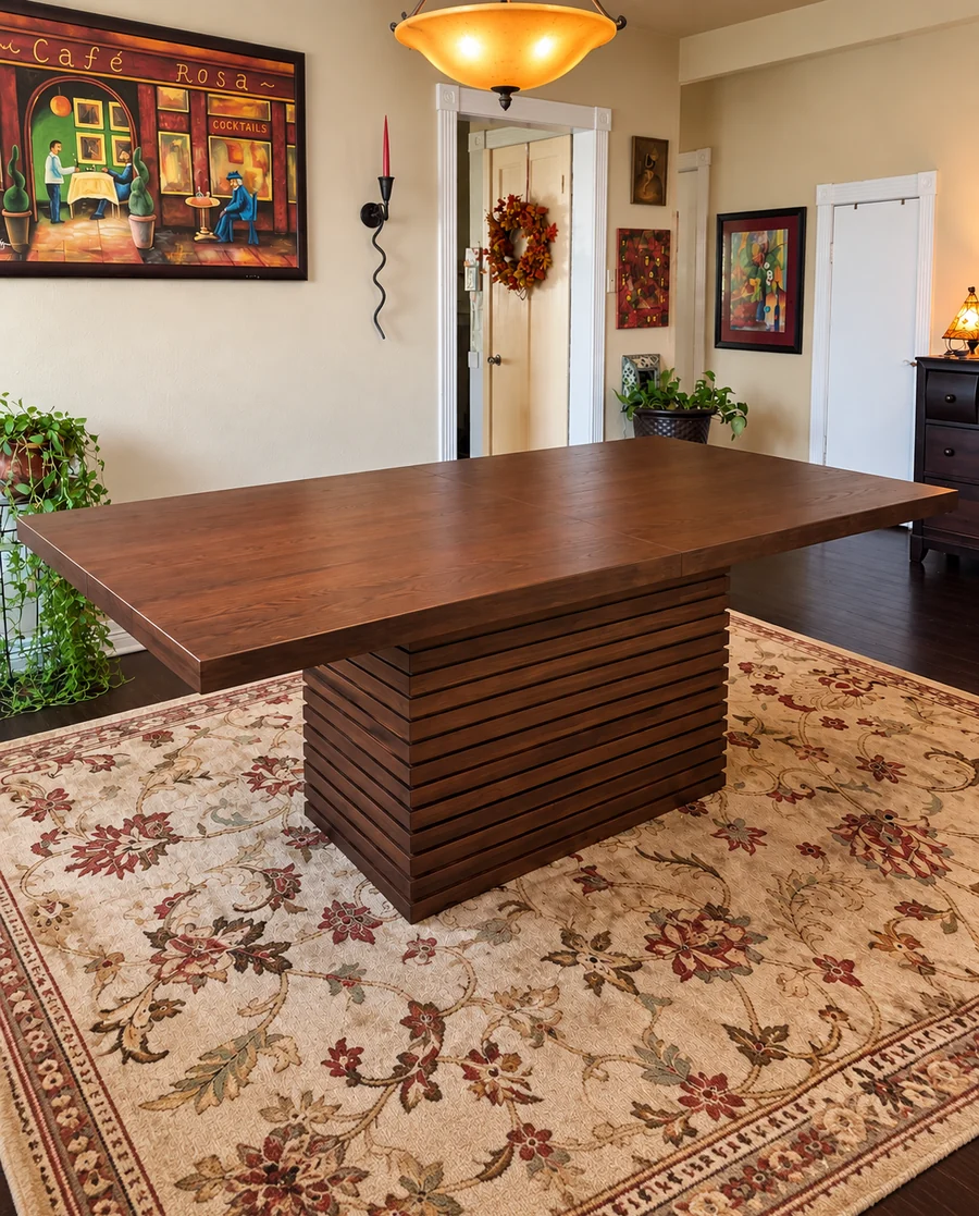 A large walnut dining table with its chairs, built and set on a rug.