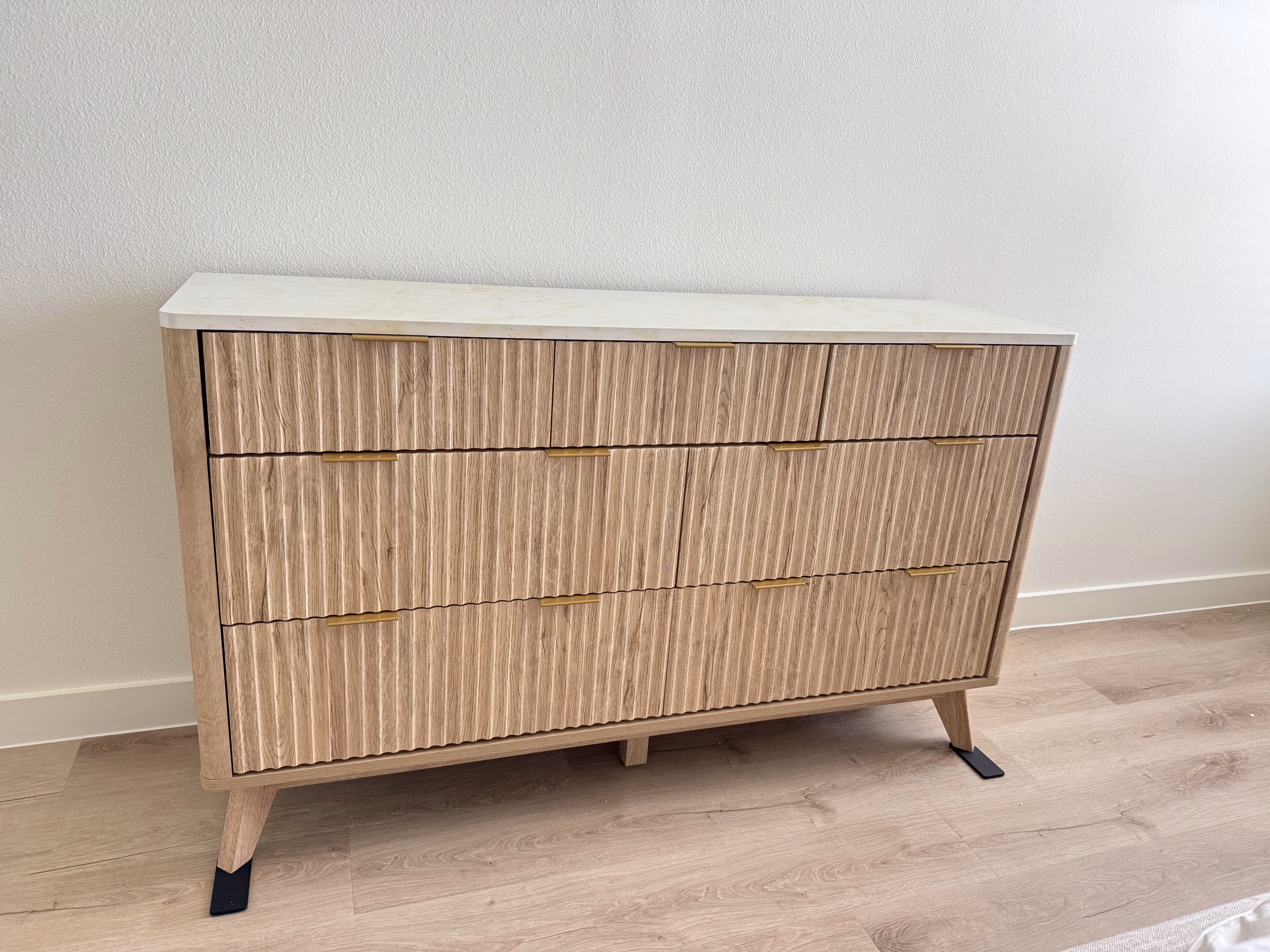 A fluted oak dresser with a stone top, assembled in a bedroom.