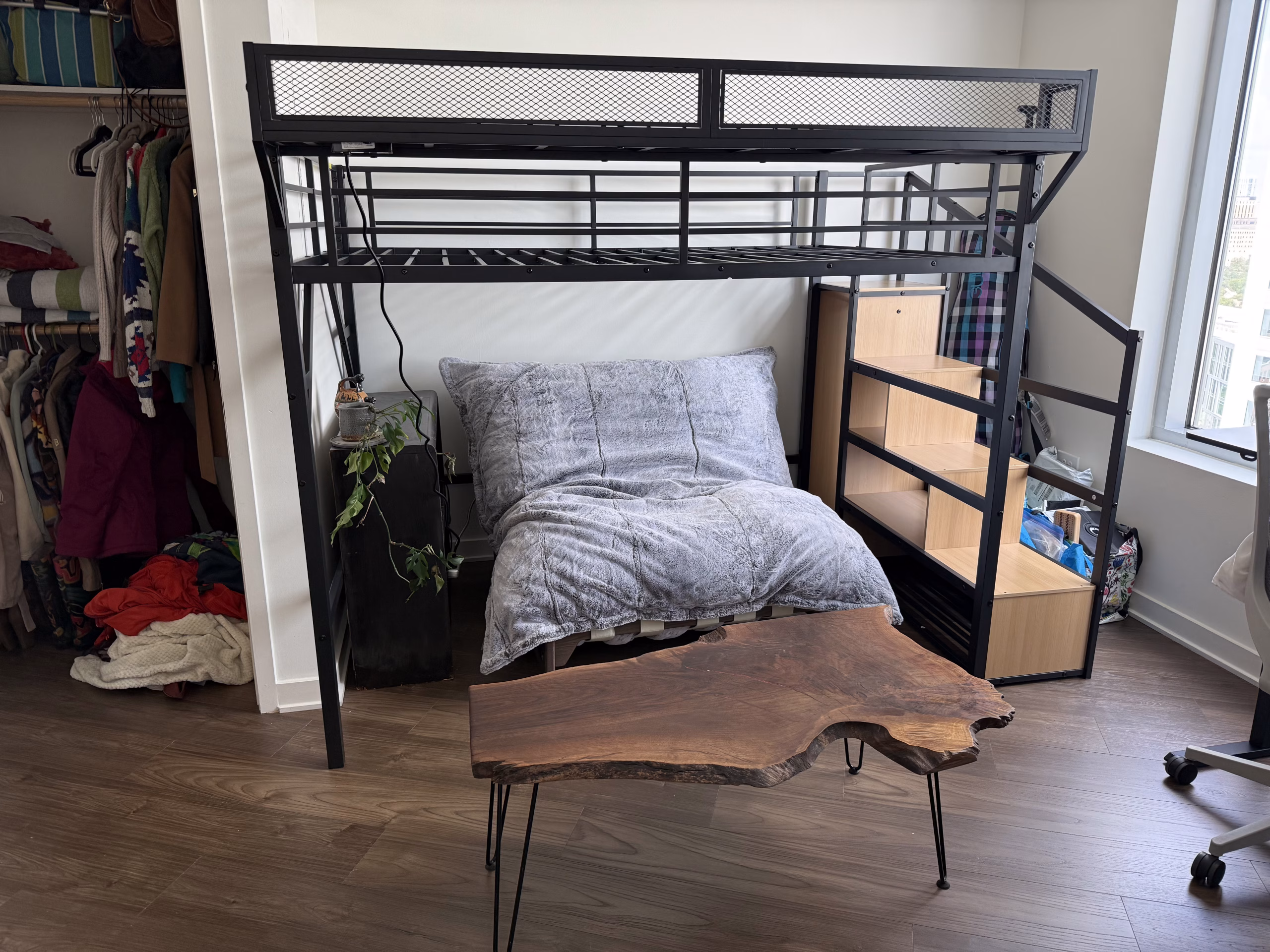 A steel loft bed with a desk and shelving underneath the raised platform, assembled in a bedroom that is already in use.