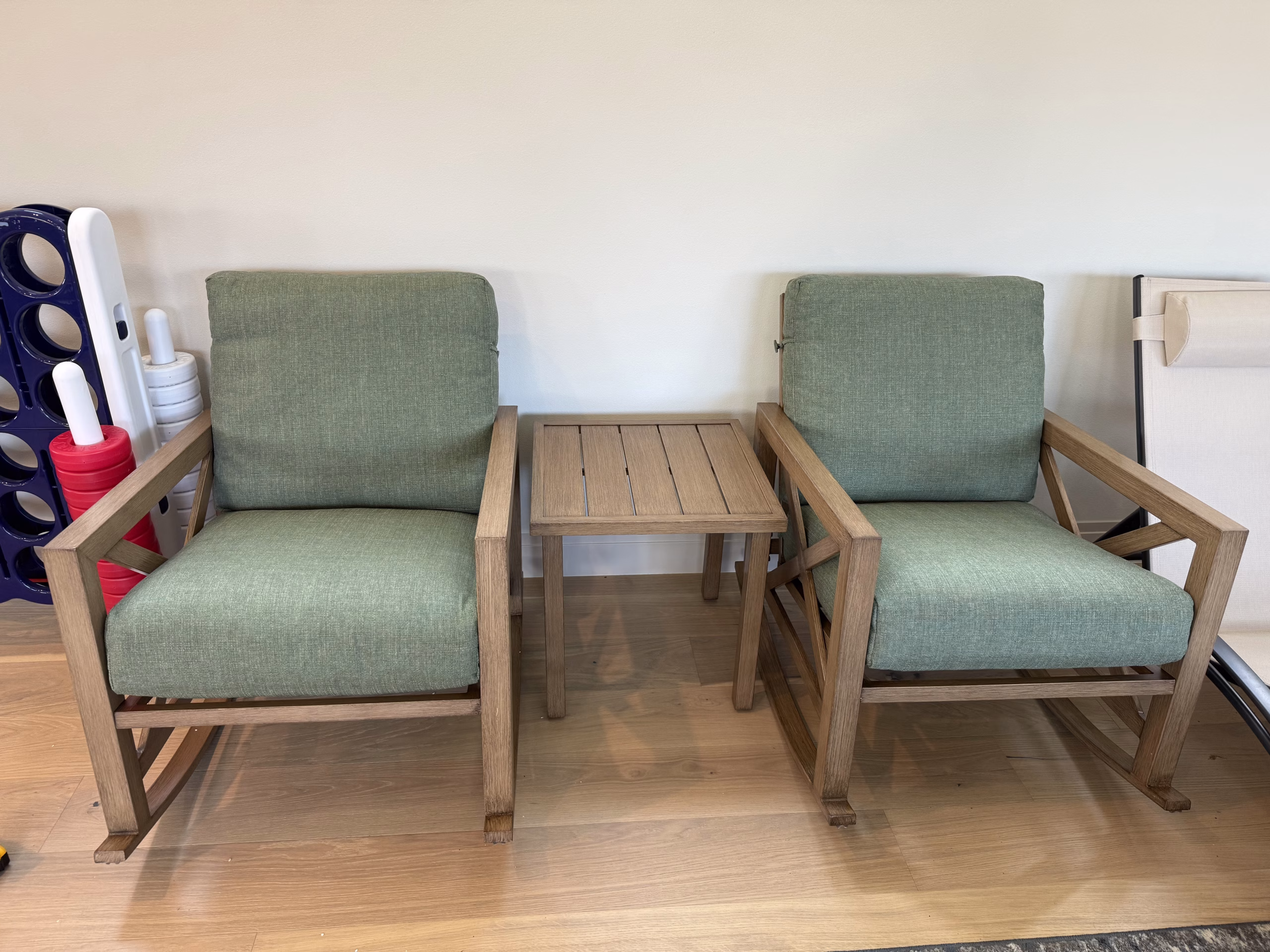 Two patio lounge chairs with a slatted side table between them, assembled outdoors against a wall.